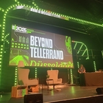 Beyond Telllerrand conference stage illuminated in neon green bulbs with two comfy chairs on stage