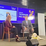 Two panel members at TechShare Pro sit on stage with a white labrador guide dog