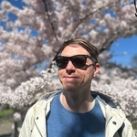 Calum wearing sun glasses shaded by a blossoming white tree