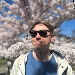 Calum wearing sun glasses shaded by a blossoming white tree