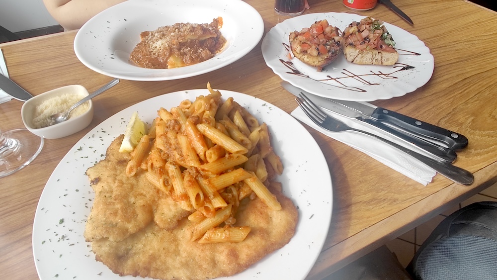 3 plates of food including chicken Milanese topped with bolognese and penne pasta, bruchetta, raviolli and parmesan on the side
