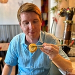 Calum holding a piece of sushi with chopsticks