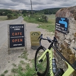 Bright yellow Canyon bicycle propped against a stone wall in the Sussex countryside and a sign pointing to Cadence Clubhouse cafe open 7 days