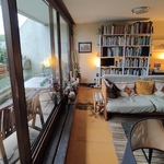 Interior of a modernist apartment with large sofa and many bookcase beside large bay windows and a balcony