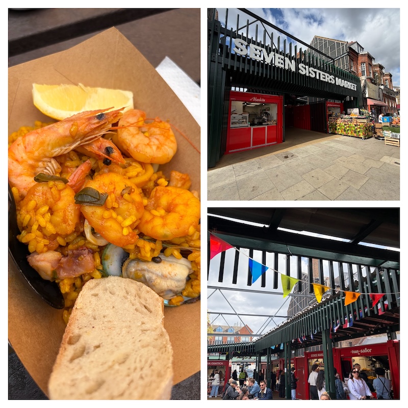 Collage of three photos from Seven Sisters Market: entrance with stalls and produce outside; lively indoor scene with flags, people, and red stalls; and a close-up of seafood paella with shrimp, mussels, lemon wedge, and bread.