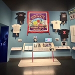Exhibition wall with large banner, t-shirts and interpretation board bneaths