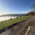 Slightly muddy path beside a steep drop hil and cloud clearing to reveal Dorking
