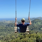 Back facing view of Calum on a swing appearing to be thrown in to the hills and ocean of Chiloe