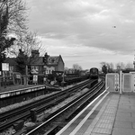 A London Underground speeds away from a over ground station and plane crosses above
