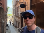 Calum wearing sun glasses with backdrop of narrow street heading down to waterfront
