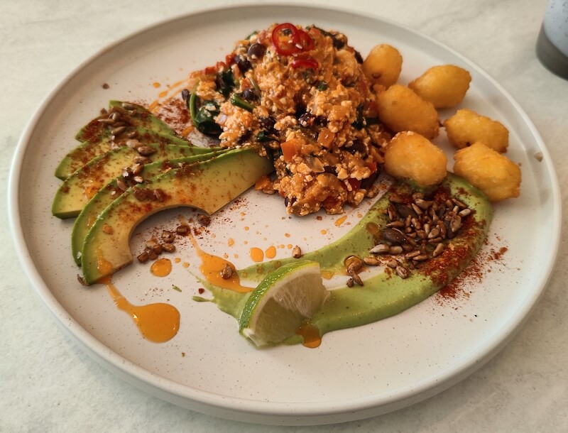 Round plate of paprika spiced tofu, black beans and spinach with avocado and potato rosti