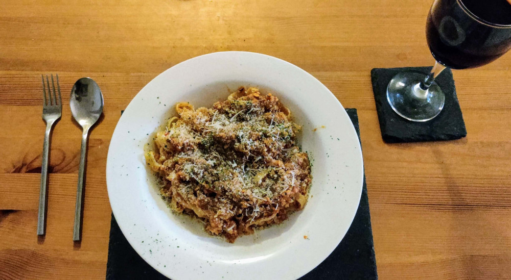 Tagliatelle cauliflower lentil bolognese in circular plate with wine on a wooden table
