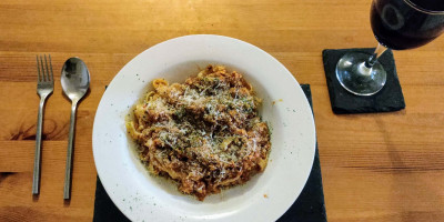 Tagliatelle cauliflower lentil bolognese in circular plate with wine on a wooden table