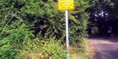 Yellow signpost - cyclists dismount to cross bridge on roadside