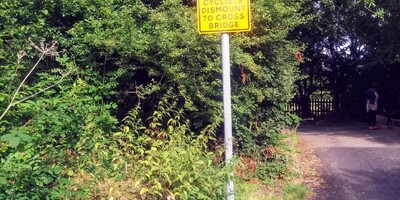 Yellow signpost - cyclists dismount to cross bridge on roadside