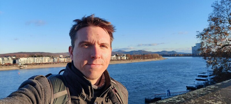 Calum profile shot with backdrop of Rhine river and hills in Bonn with clear blue sky