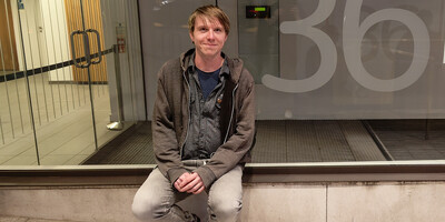 Calum sitting beside an office entrance window with the figure 36 printed on the glass