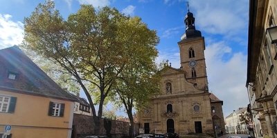 Bright coloured orthodox-style church with tower in foreground and trees beside