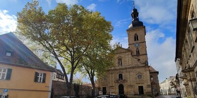 Bright coloured orthodox-style church with tower in foreground and trees beside