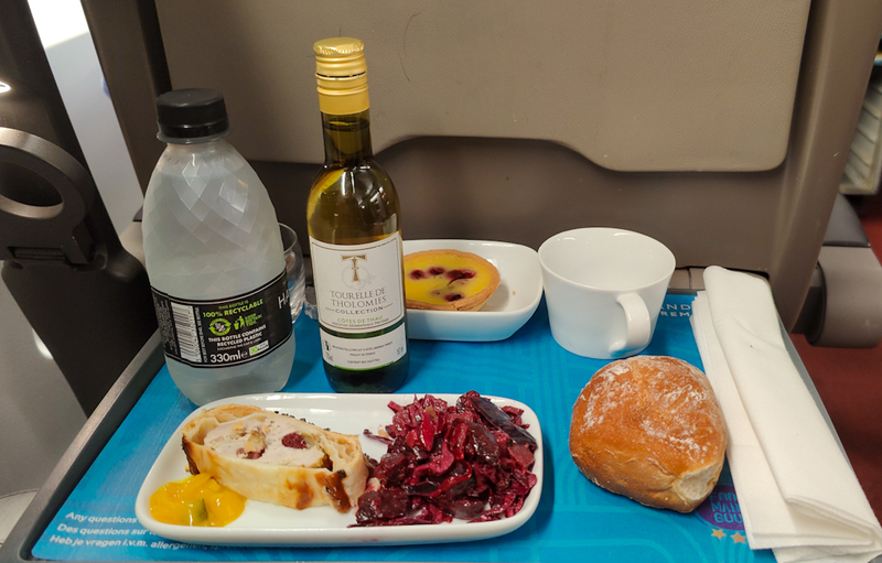 chicken roulade dish, white wine, bread, water bottle and tart on a blue tray