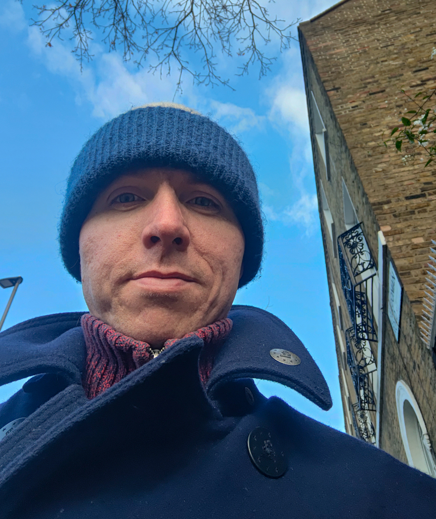 Calum wearing a blue beanie with backdrop of clear blue sky and corner of a typical terraced house in London