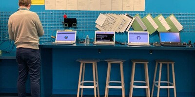 man stands at a blue counter displaying multiple laptops, and accessibility personas described on posters above