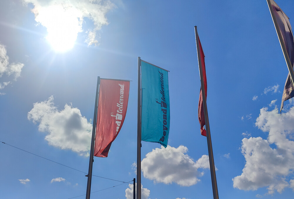 Beyond Tellerrand flags to the backdrop of a clear blue sky and flaring sunshine