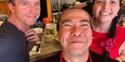 Calum and Mena smiling alongside the owner of a restuarant in a selfie pose