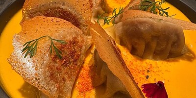 Gyosas in a bright yellow sauce and decorated with flours and parsley