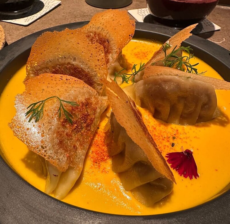 Gyosas in a bright yellow sauce and decorated with flours and parsley